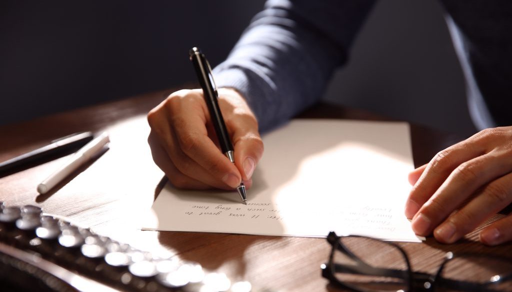 Man writing letter at wooden table indoors, closeup