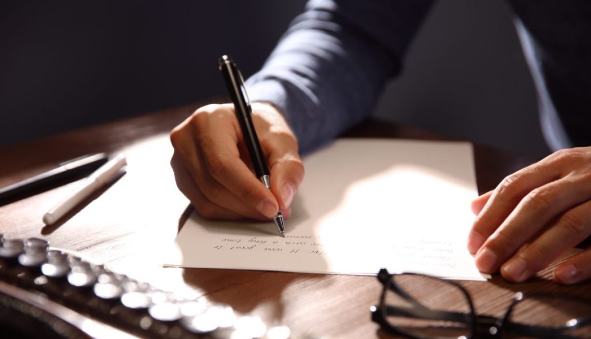 Man writing letter at wooden table indoors, closeup