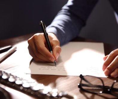Man writing letter at wooden table indoors, closeup